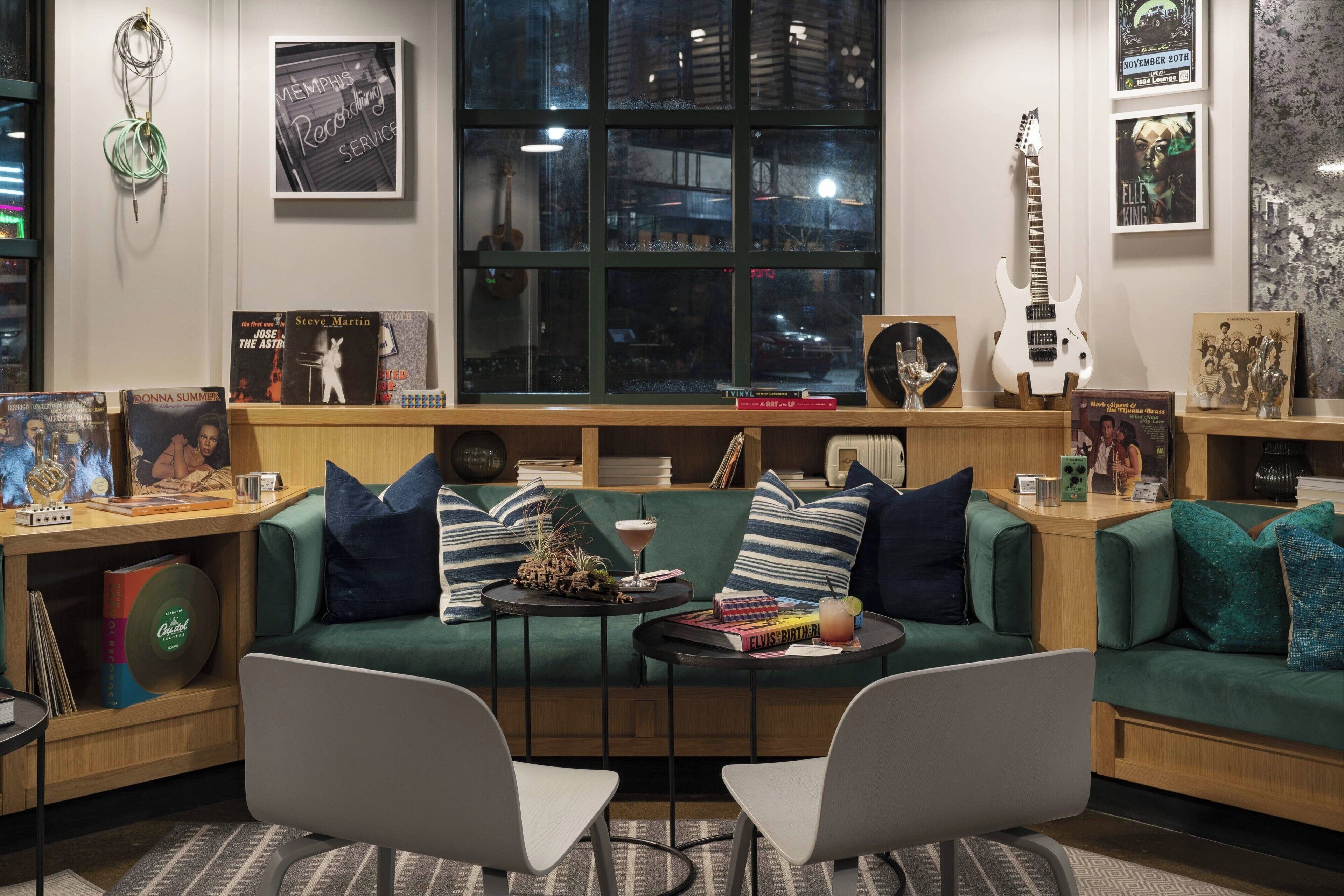 Een gezellige woonkamer met een groene bank, twee witte stoelen, een salontafel en een raam met uitzicht op de stad.