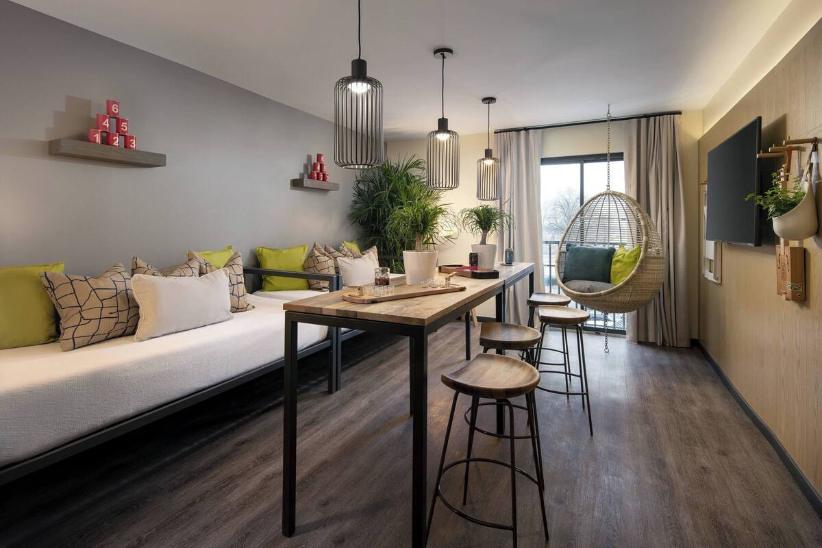 A modern living room with a sofa, hanging chairs, a wooden table, and a TV mounted on the wall.