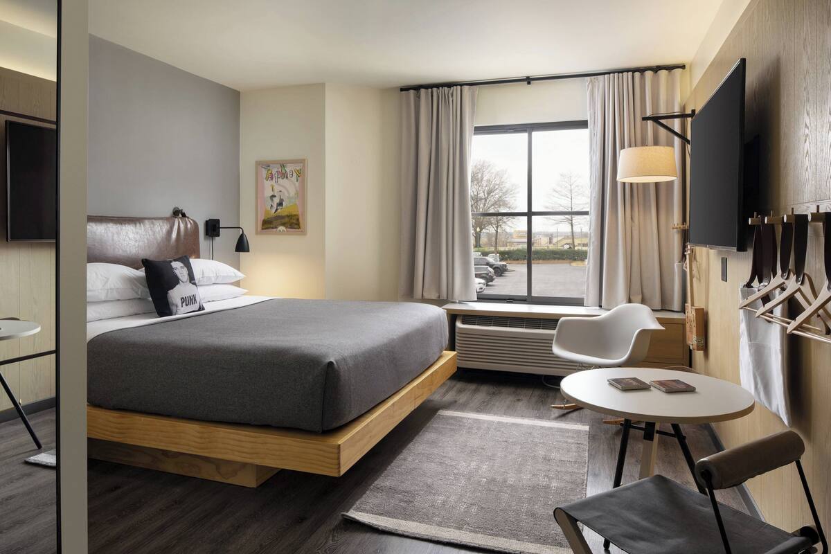 A modern hotel room with a bed, a desk, a chair, a TV, and a window with curtains.