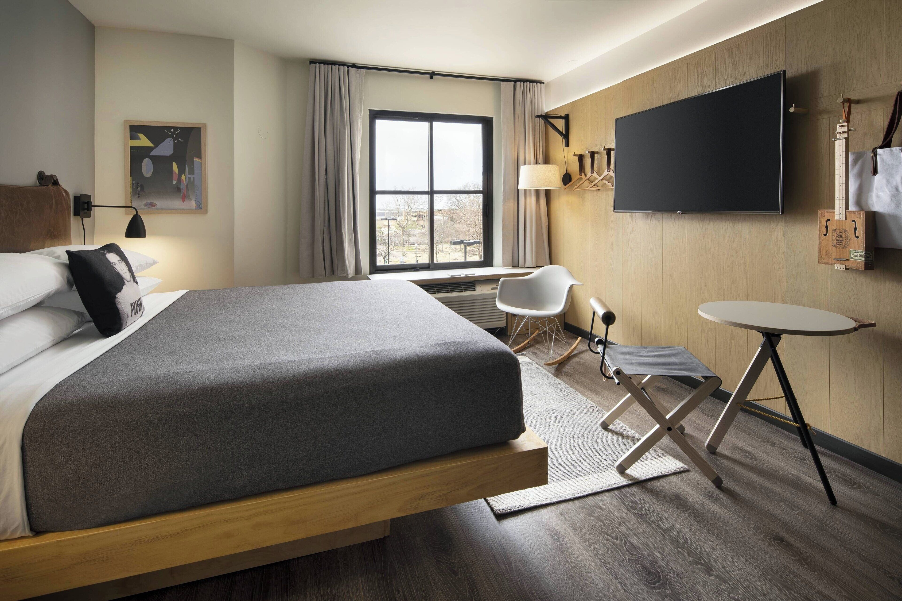 Una habitación de hotel moderna con una cama grande, un televisor de pantalla plana, un escritorio y una silla.