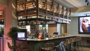 A bar area with a neon sign, multiple shelves of bottles, and wicker bar stools. - MOXY Memphis Downtown (Memphis)