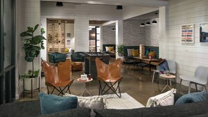 A modern living room with a sofa, leather chairs, a coffee table, and a foosball table. - MOXY Memphis Downtown (Memphis)