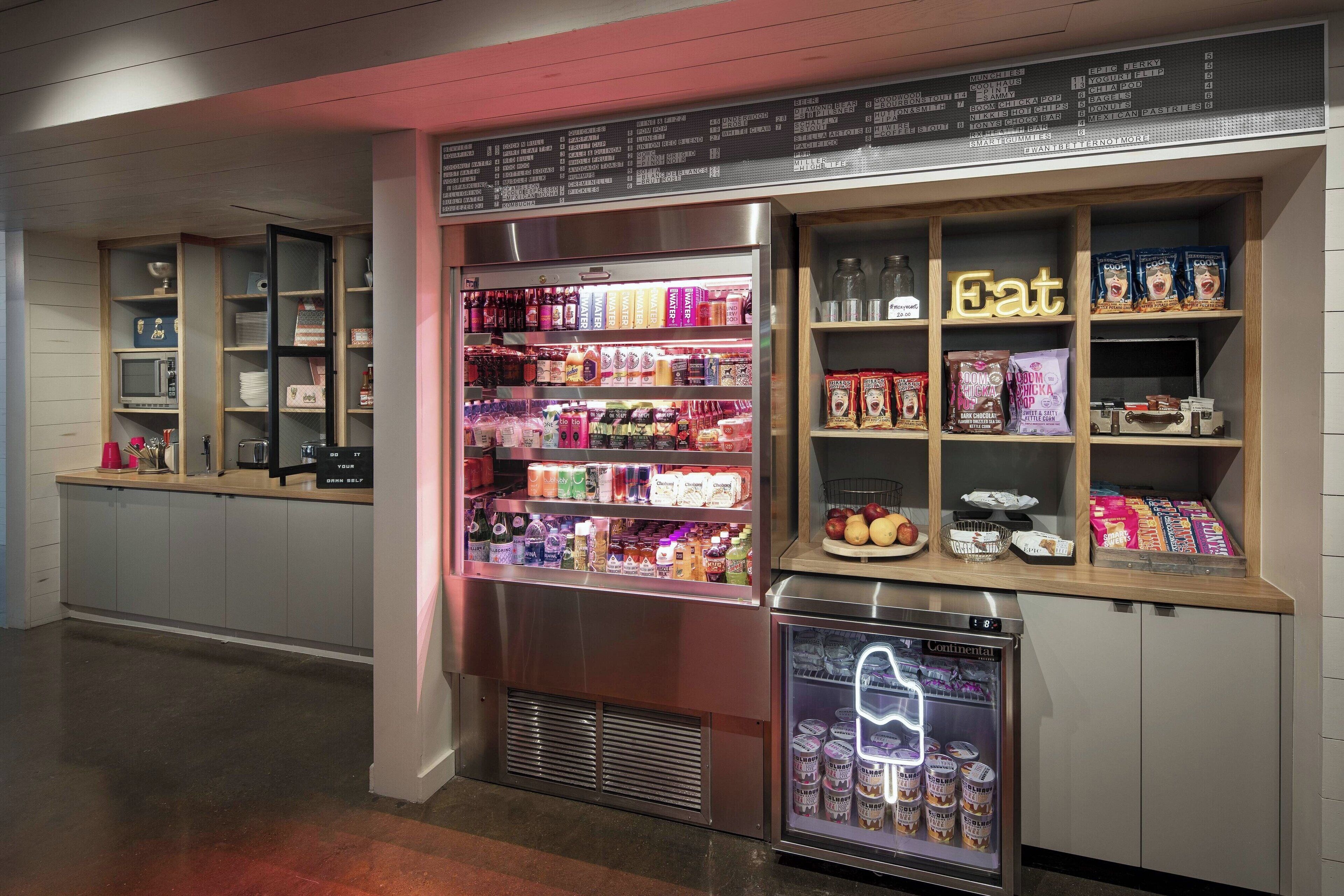 A self-service beverage station with refrigerated drinks and snacks, a microwave, and a small refrigerator.