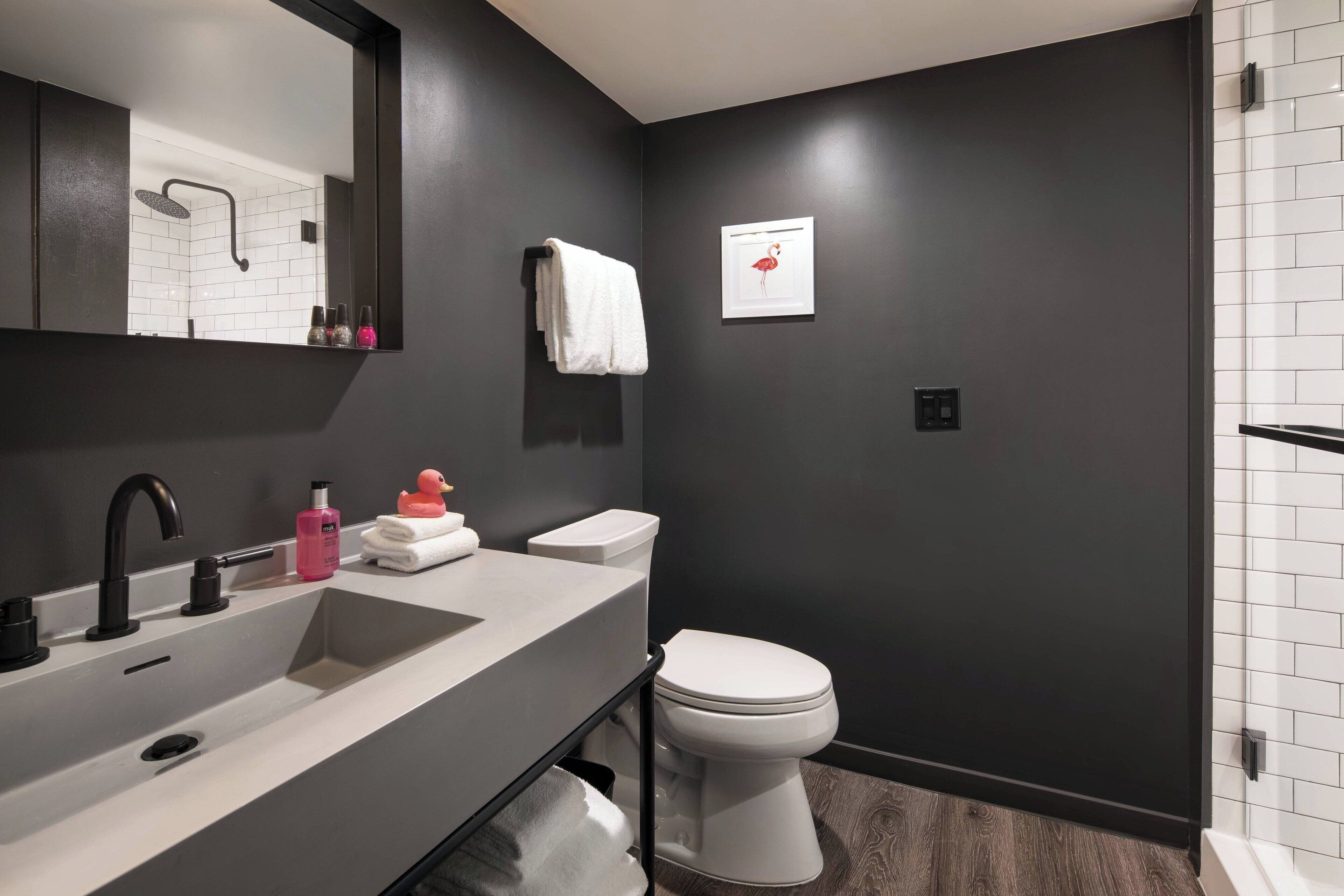 A modern bathroom with a dark wall, a white sink, a toilet, and a shower.