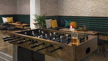 Una mesa de fútbol de mesa en un área de descanso moderna con un sofá y sillones, una planta y una mesa con una cerveza.