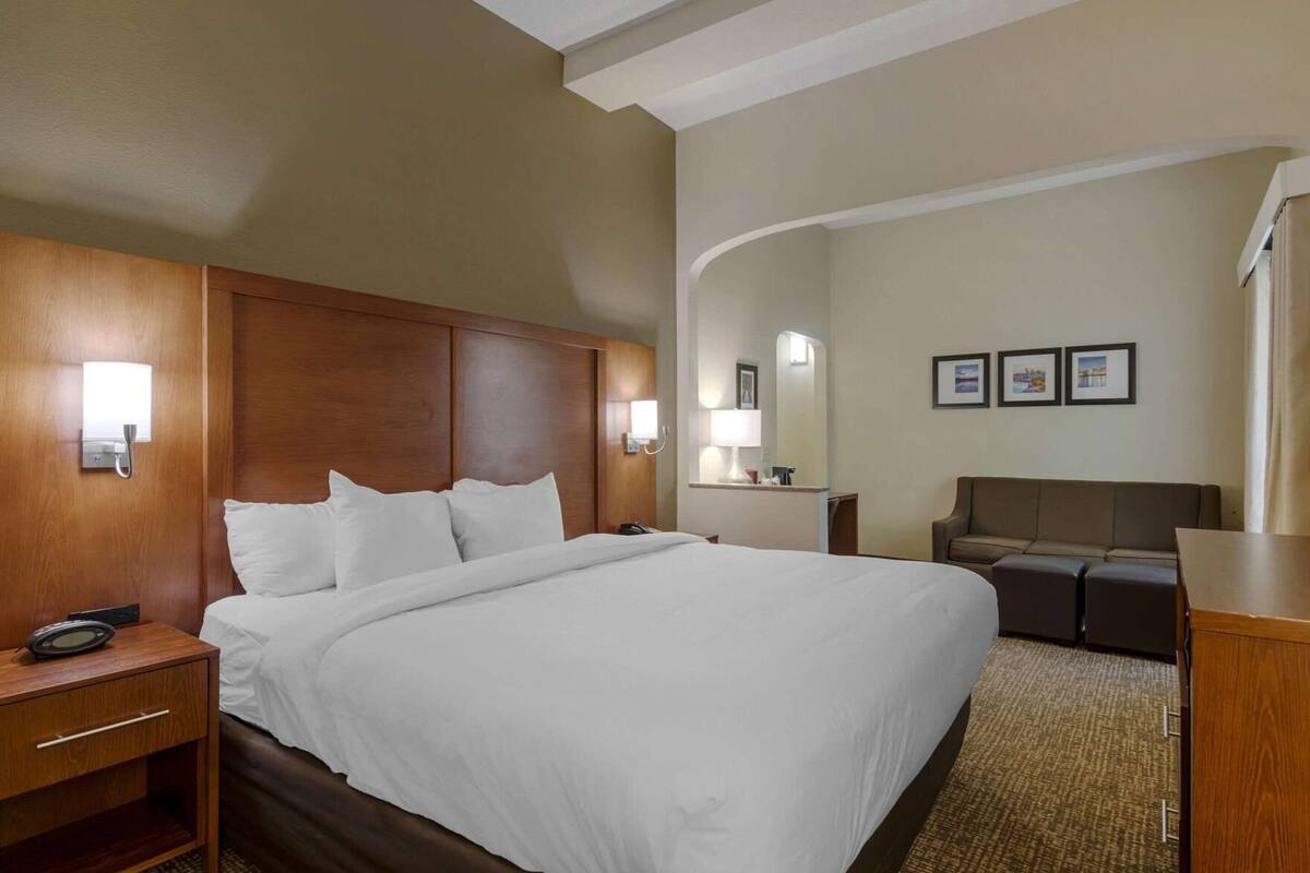 Habitación de hotel con una cama grande, mesitas de noche, un escritorio, una silla y un pequeño sofá.