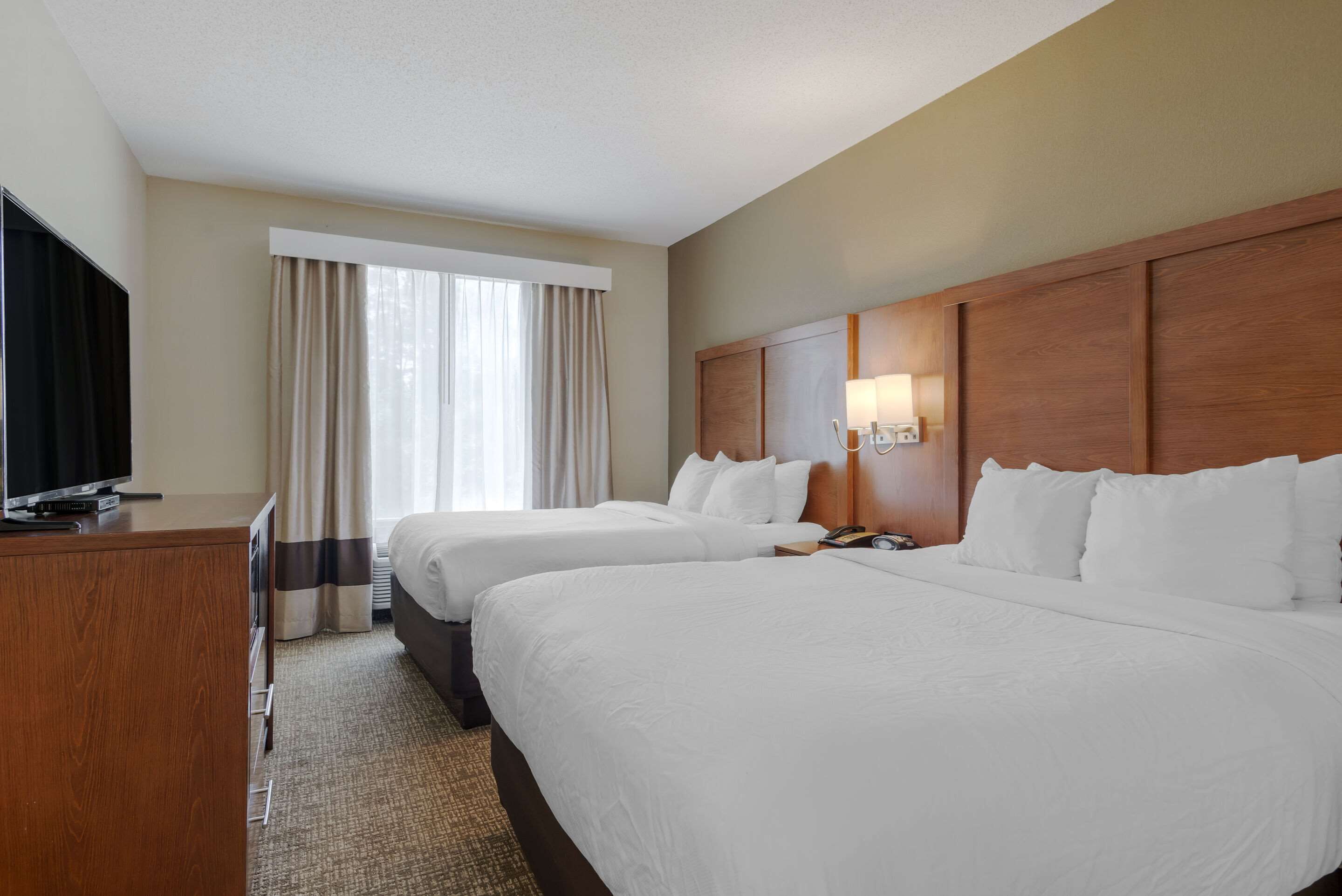 A hotel room with two beds, a TV, a desk, and a window with curtains.