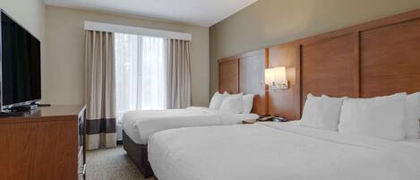 A hotel room with two beds, a TV, a desk, and a window with curtains.