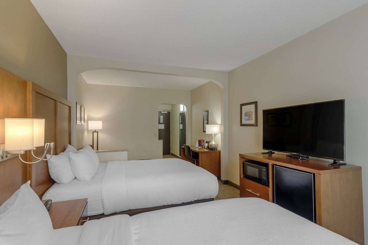 Habitación de hotel con dos camas, televisión, escritorio con lámpara, microondas y refrigerador.