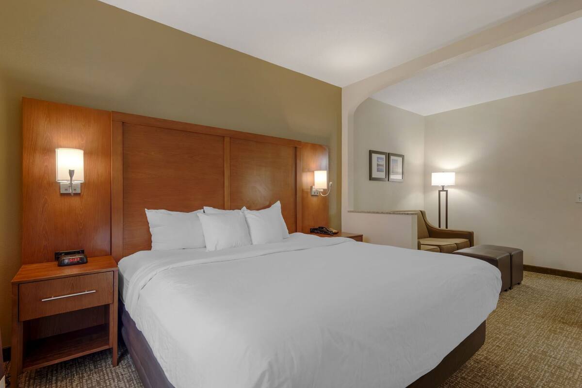 Una habitación de hotel con una cama grande, cabecera de madera, mesitas de noche, escritorio, silla y lámpara.