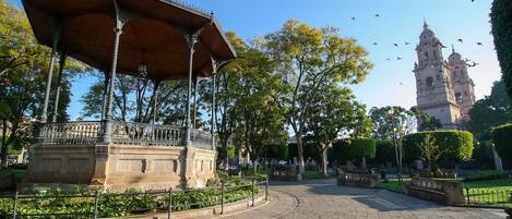 Un parque con un pabellón, una fuente y un edificio histórico al fondo.