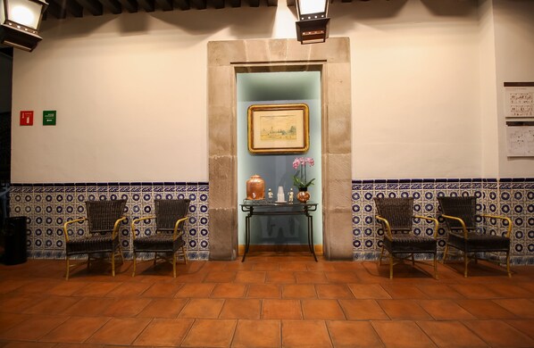 Un vestíbulo con suelo de baldosas, dos sillones de mimbre, una mesita con objetos decorativos y un cuadro en la pared.