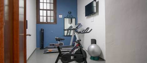Un gimnasio con equipo de ejercicio, un espejo, un televisor y una ventana.