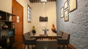 A dining area with a wooden table, four chairs, a TV above the table, and a textured wall with framed pictures.