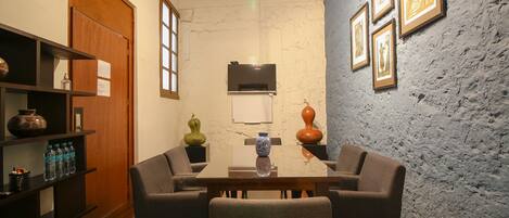 A dining area with a wooden table, four chairs, a TV above the table, and a textured wall with framed pictures.