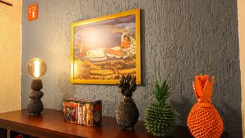 Un mur orné d’un tableau encadré, une lampe à lave, une boîte de jeux de société sur le thème du Mexique, un vase en forme d’ananas et une plante d’ananas.