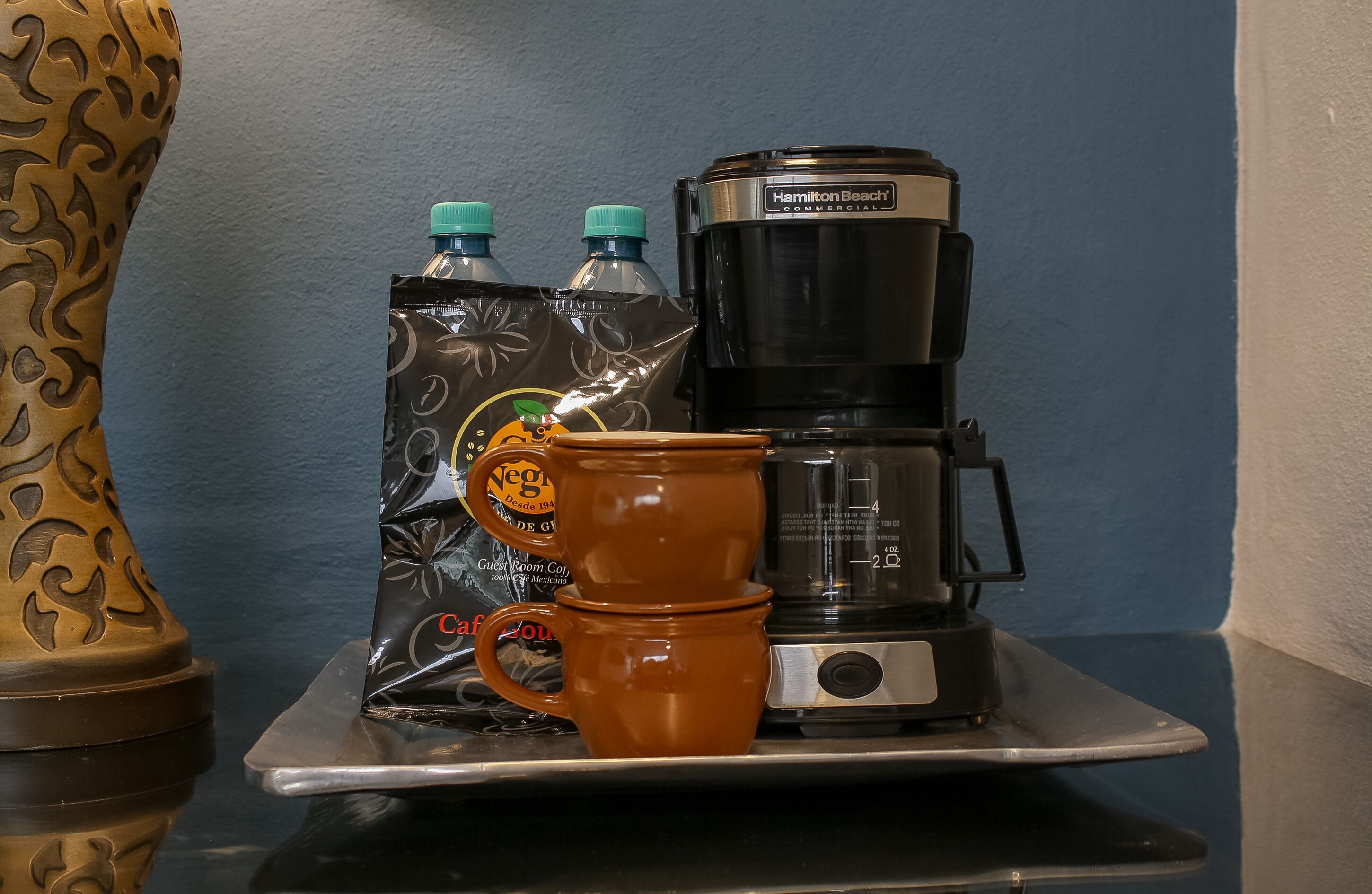 Una cafetera, dos botellas de agua y dos tazas de café sobre una bandeja.