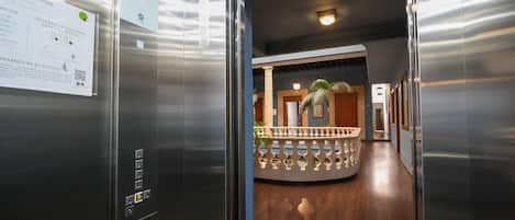 An elevator interior with a sign, a control panel, and a view of a lobby with a wooden floor and a decorative railing.