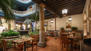 A restaurant with wooden tables and chairs, potted plants, and a tiled floor.