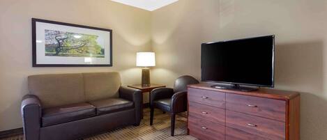 A hotel room with a sofa, a television on a wooden cabinet, a lamp, and a framed picture on the wall.