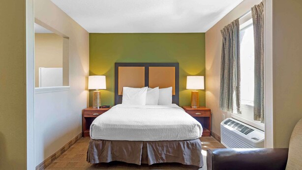 Una habitación de hotel con una cama grande, dos mesitas de noche con lámparas, una ventana con cortinas y un equipo de aire acondicionado.