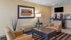 Habitación de hotel con un cartel de 'WELCOME', una estación de café, un televisor y una zona de estar con una mesa y sillas.