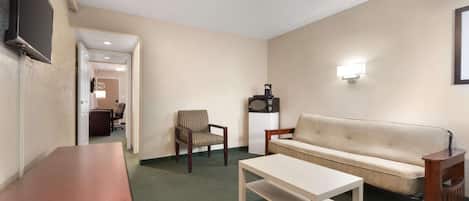 A hotel room with a flat-screen TV, a sofa, a chair, a coffee table, and a desk.