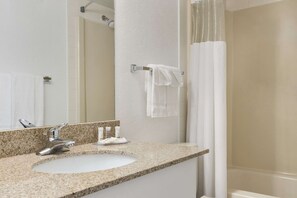 A bathroom with a granite countertop sink, a mirror, a towel rack, and a shower curtain.