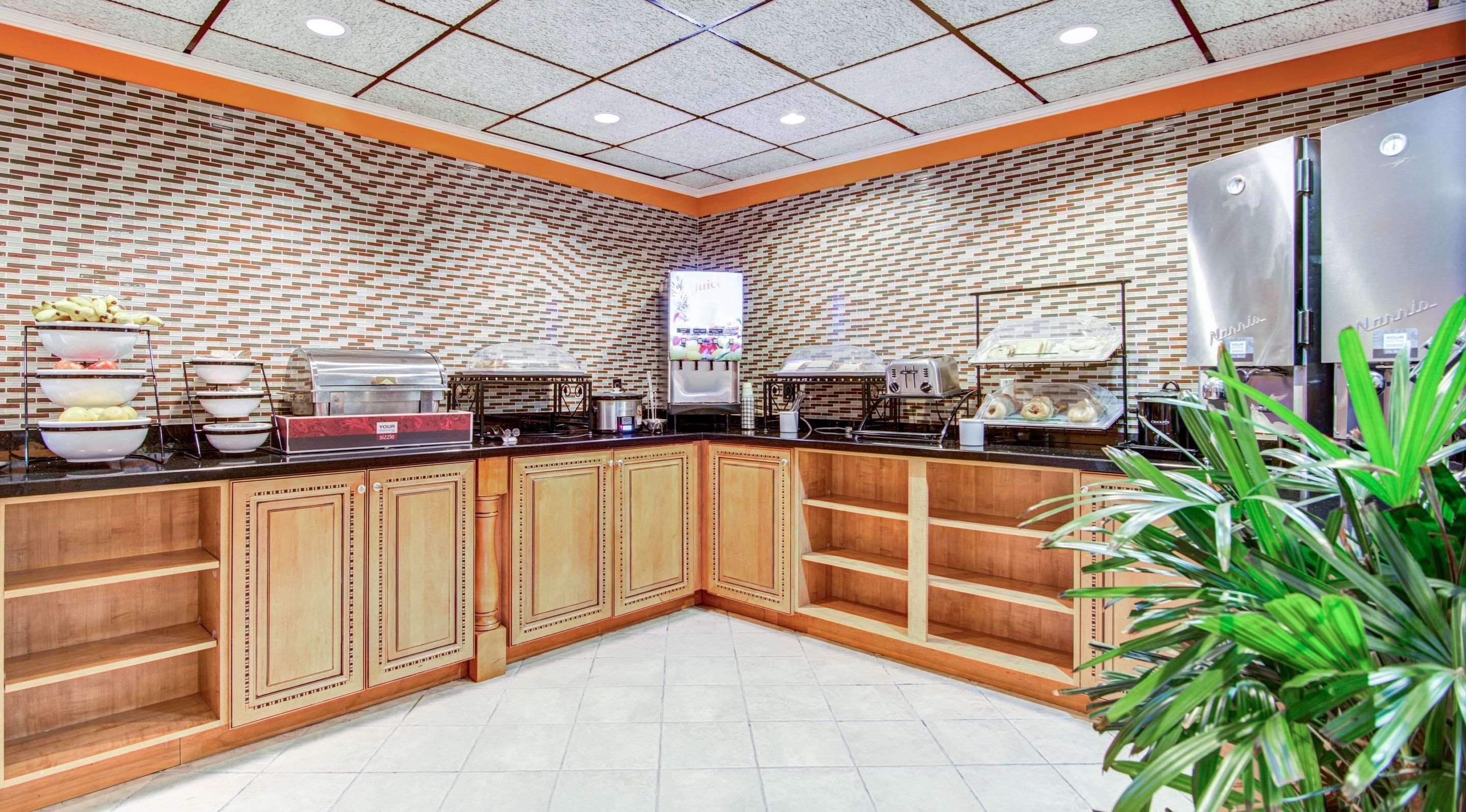 A buffet setup with a brick-patterned wall, a stainless steel refrigerator, and a juice dispenser.