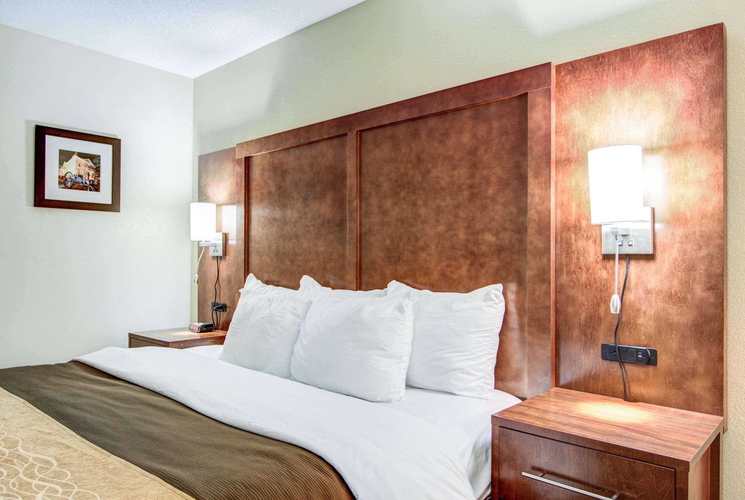 A hotel room with a large bed, wooden headboard, bedside lamps, and a nightstand with a lamp.