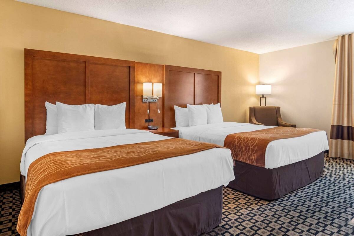 A hotel room with two beds, a wooden headboard, a nightstand with a lamp, and a patterned floor.