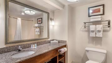 A modern bathroom with a granite countertop sink, a large mirror, a toilet, and a towel rack.