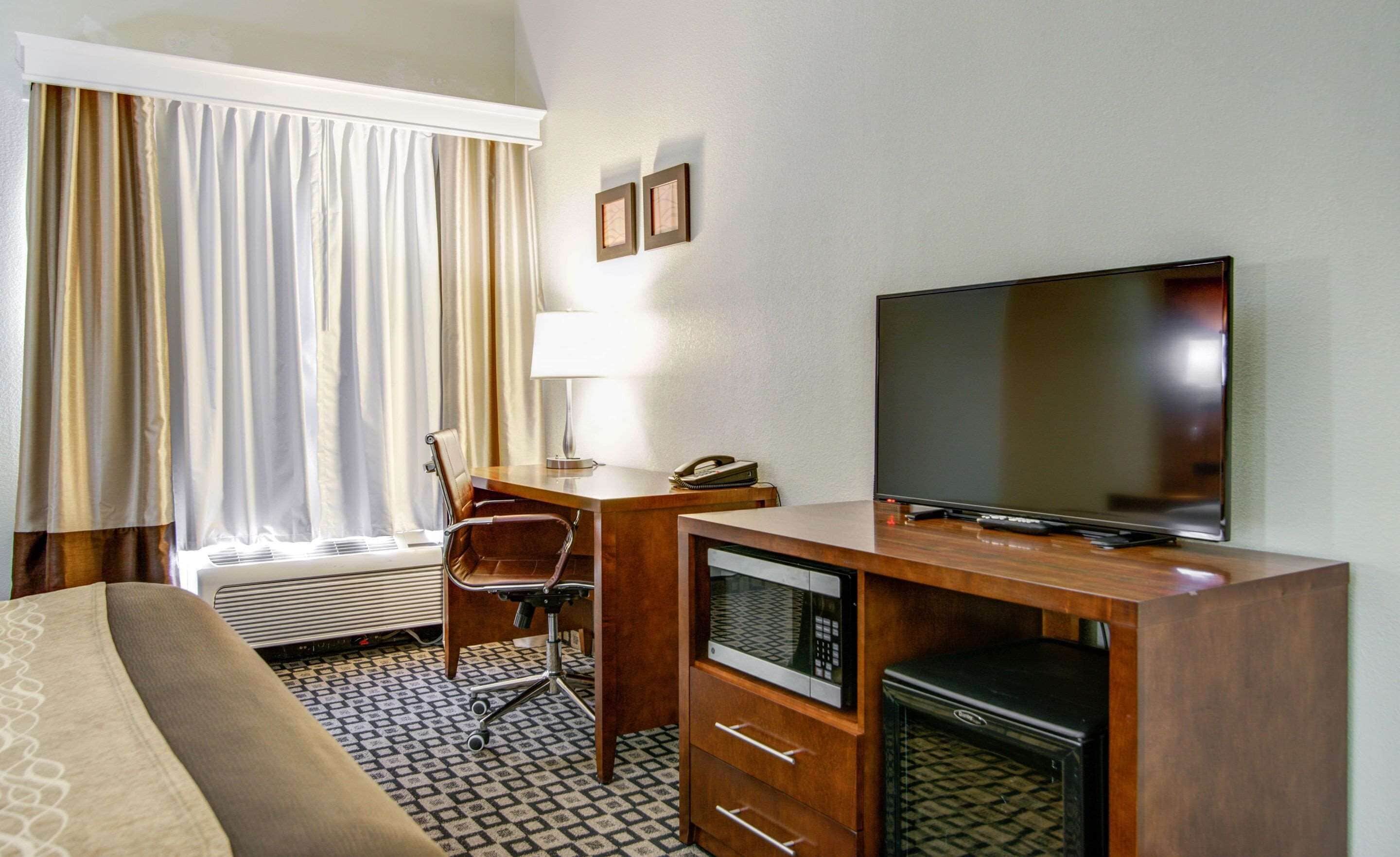 A hotel room with a bed, a desk with a lamp, a TV, a microwave, and a chair.