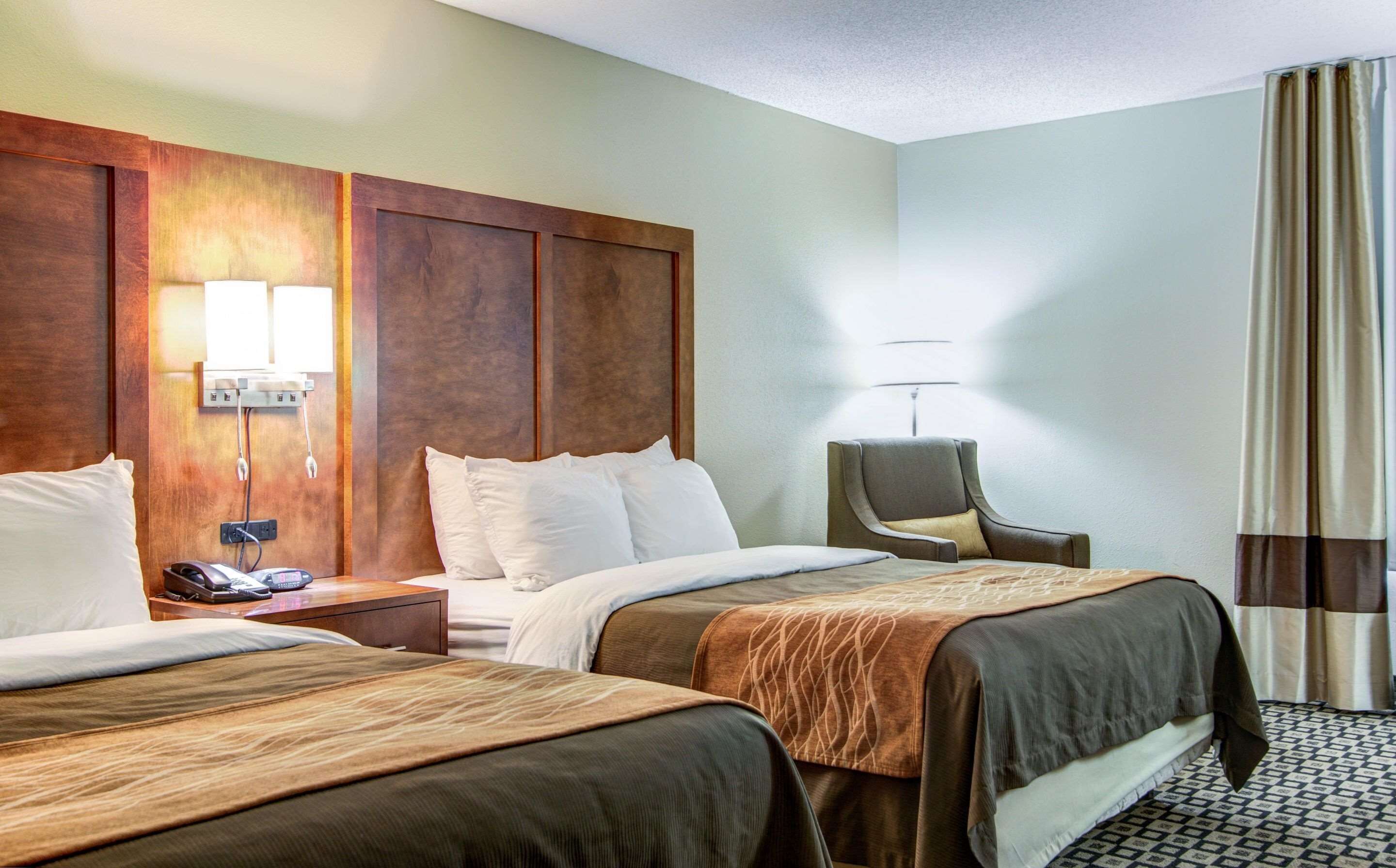 Une chambre d’hôtel avec deux lits, une tête de lit en bois, un bureau avec une lampe et une chaise.