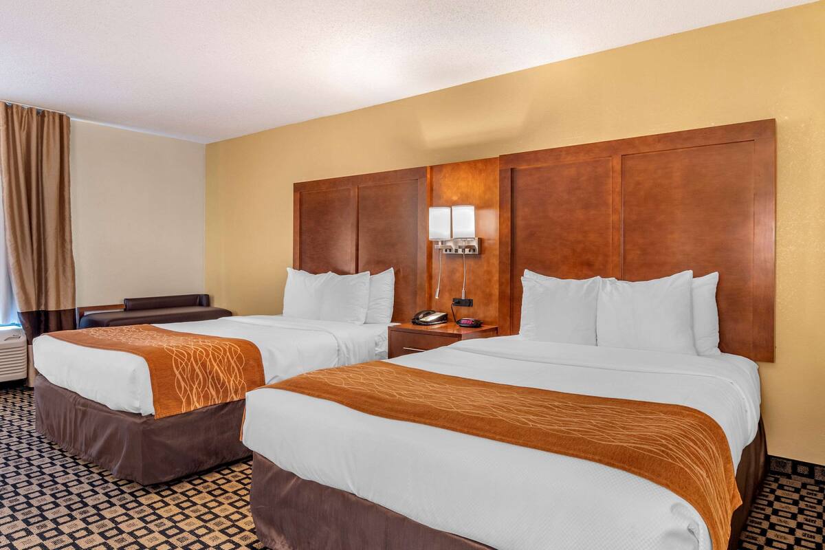 A hotel room with two beds, a large wooden headboard, a nightstand with a lamp, and a patterned floor.