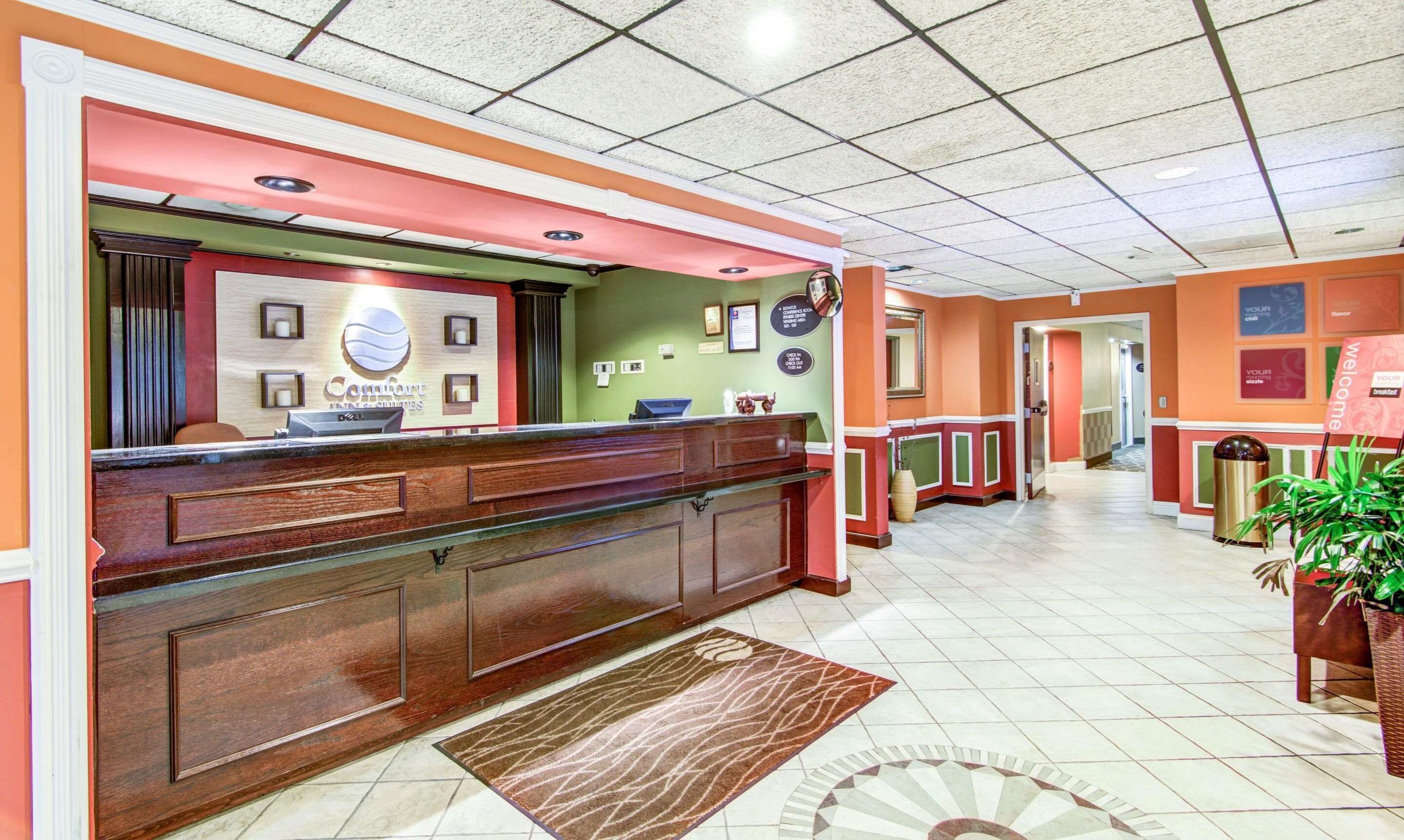 A hotel reception area with a wooden reception desk, a green wall with framed pictures, and a tiled floor.