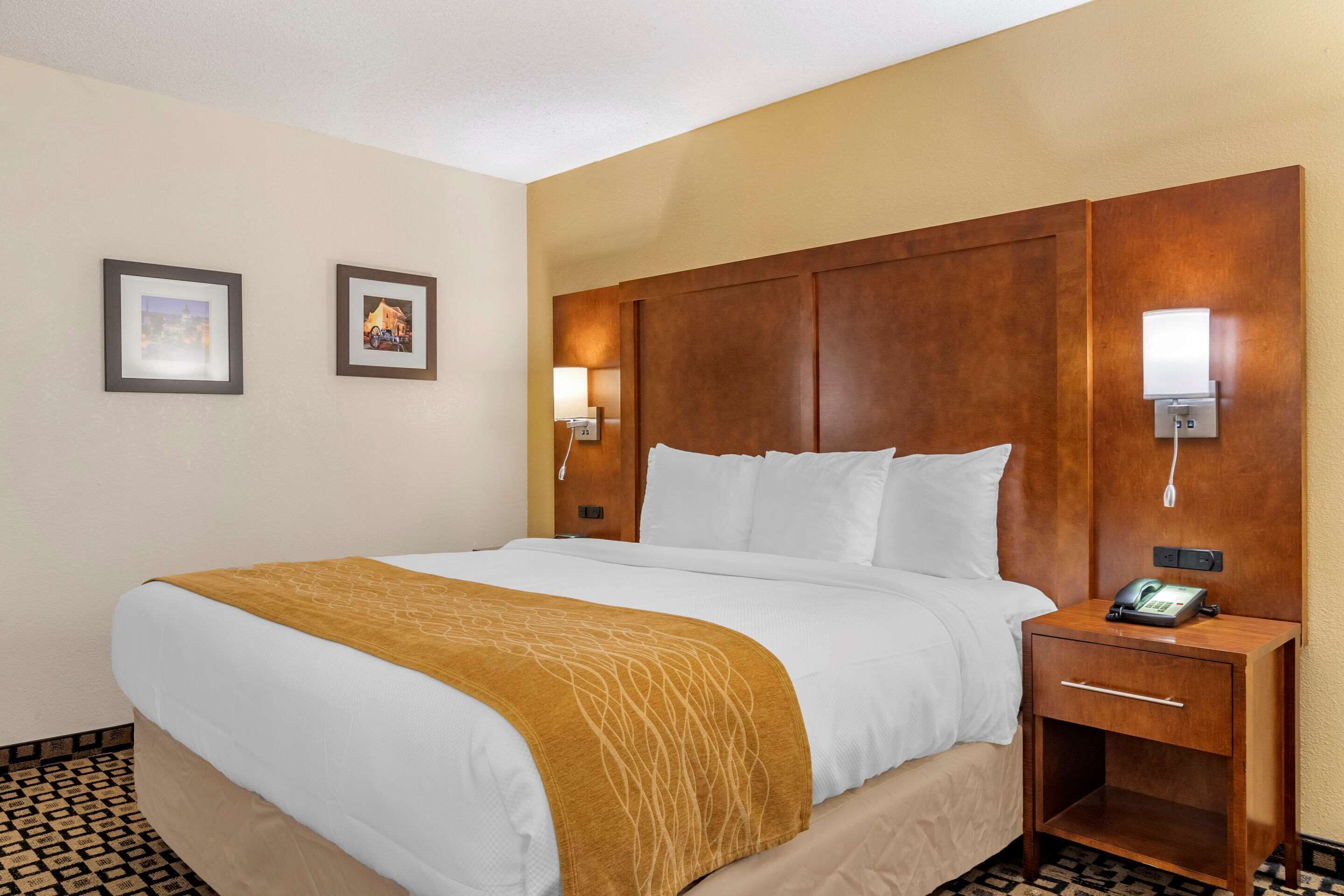 A hotel room with a large bed, a wooden headboard, two wall-mounted lights, a bedside phone, and a small wooden nightstand.