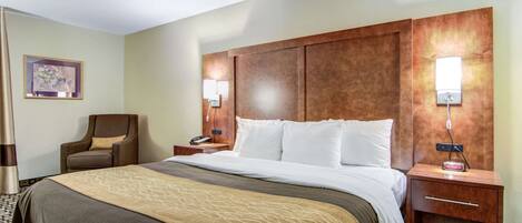 A hotel room with a large bed, a wooden headboard, two bedside tables with lamps, a chair, and a framed picture on the wall.