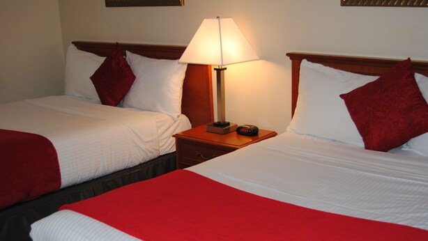 Two beds with red and white bedding, a bedside table with a lamp, and a clock.
