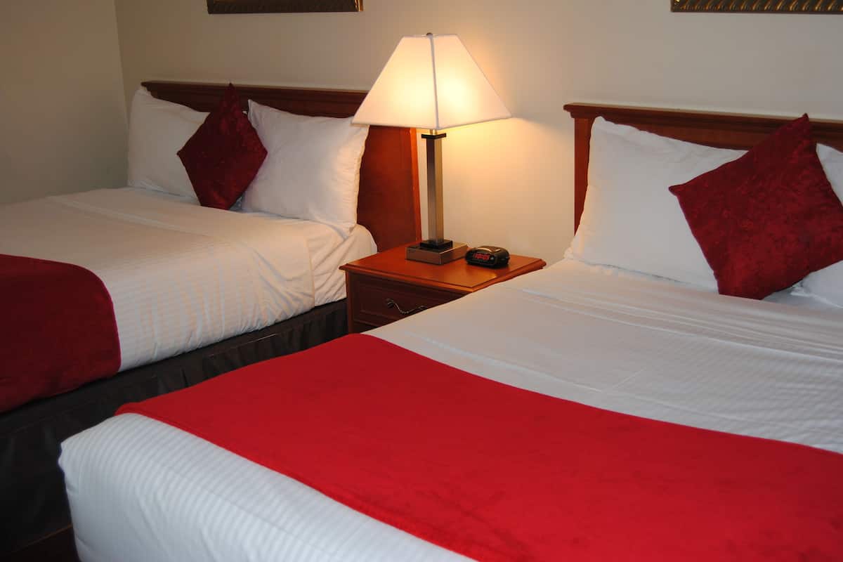 Two beds with red and white bedding, a bedside table with a lamp, and a clock.