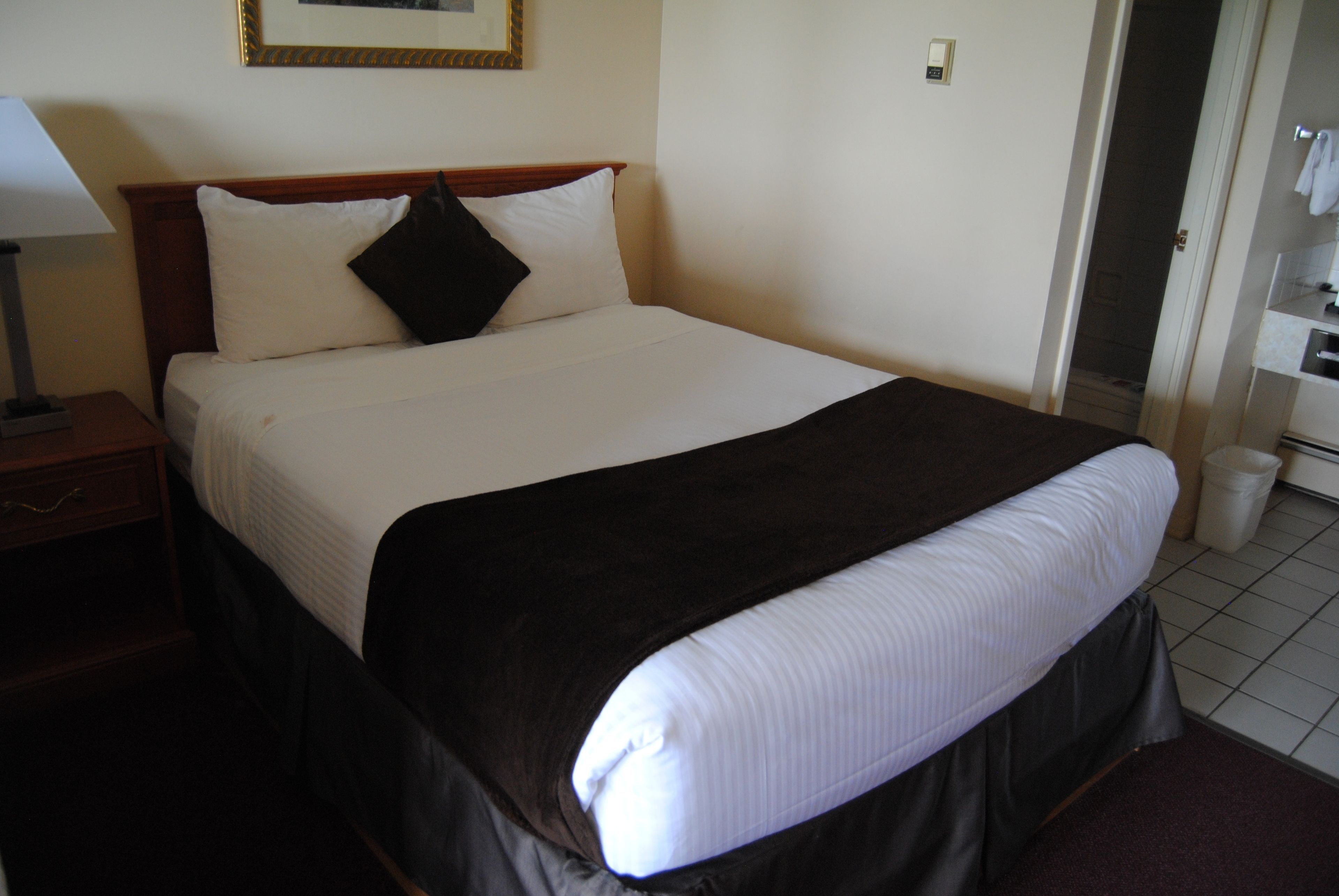 Habitación de hotel con cama, mesita de noche, lámpara y baño visible a través de una puerta abierta.