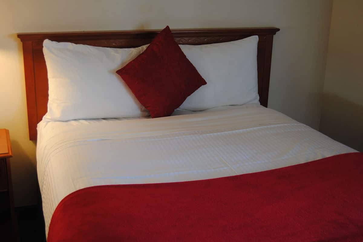 A bed with white bedding and a red throw blanket.