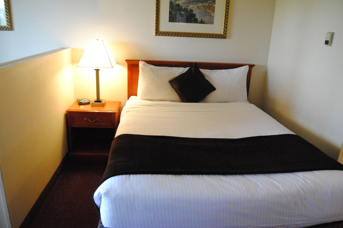 A hotel room with a neatly made bed, a bedside lamp, and a framed picture on the wall.