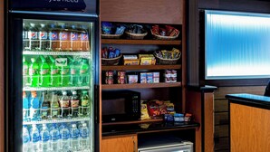 Una tienda de barrio con un refrigerador de bebidas, estantes con snacks y un televisor.