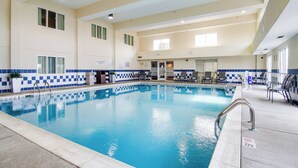 Una amplia piscina interior con agua cristalina, rodeada por una solana con baldosas y una pared a cuadros azules y blancos.
