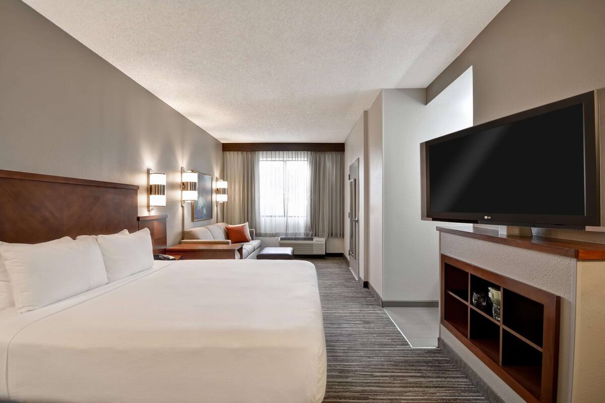 Hotelkamer met een groot bed, een flatscreen televisie, een bank, een bureau en een raam met gordijnen.