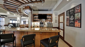Una zona de bar con mostrador de madera, tres taburetes negros, un televisor sobre el bar y una pared con pizarras de menú enmarcadas.