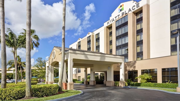 Un hotel moderno con entrada cubierta, palmeras y un cielo azul despejado.