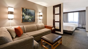 Una habitación de hotel con sofá, reposapiés, un cuadro, escritorio y cama.