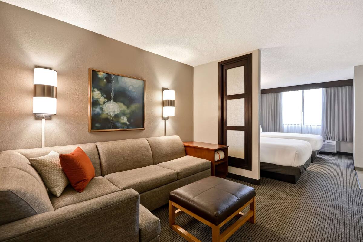 Een hotelkamer met een bank, een poef, een schilderij, een bureau en een bed.